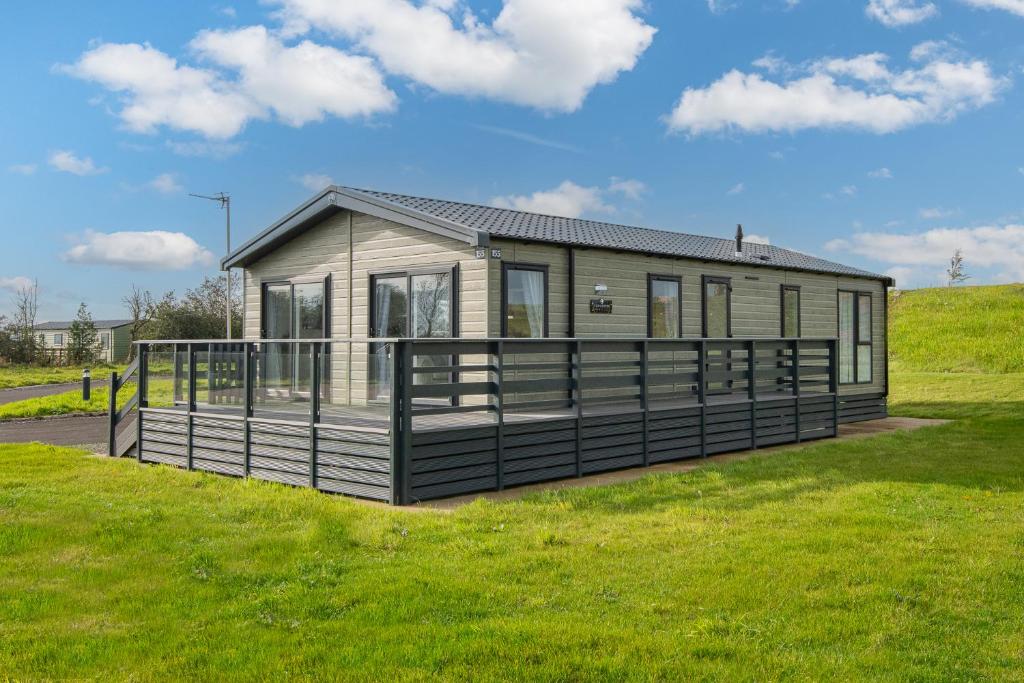 a small house with a large deck in a field at Birch Timber Holiday Lodge in Bassenthwaite