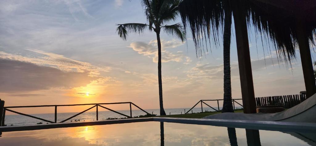 uma piscina com palmeiras e o oceano ao pôr do sol em Pousada D'Oxum Caraíva em Caraíva