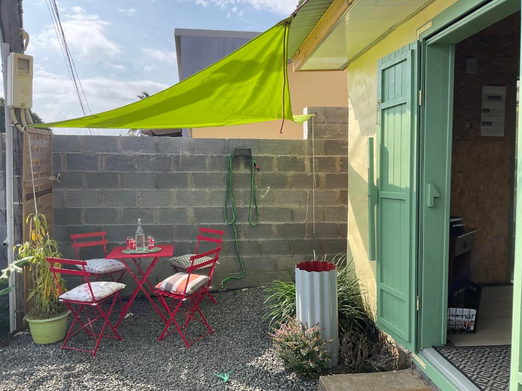 un patio con mesa, sillas y una sombrilla verde en Case créole en Saint-Pierre