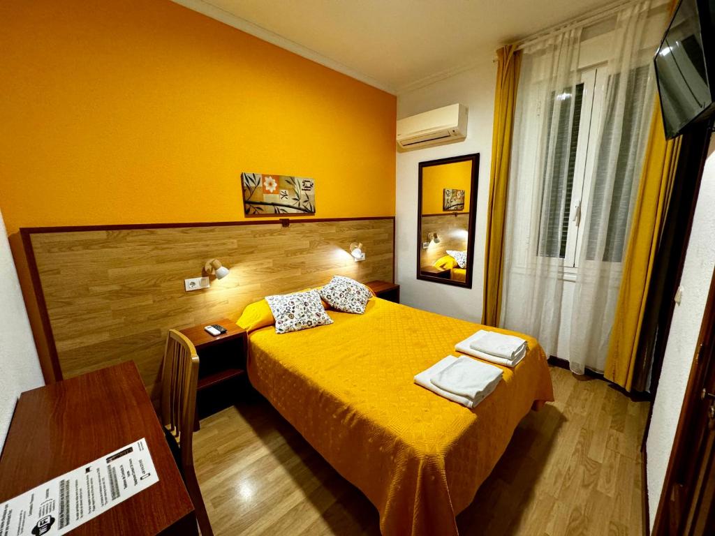 Dormitorio amarillo con cama y escritorio en Hostal Edreira, en Madrid