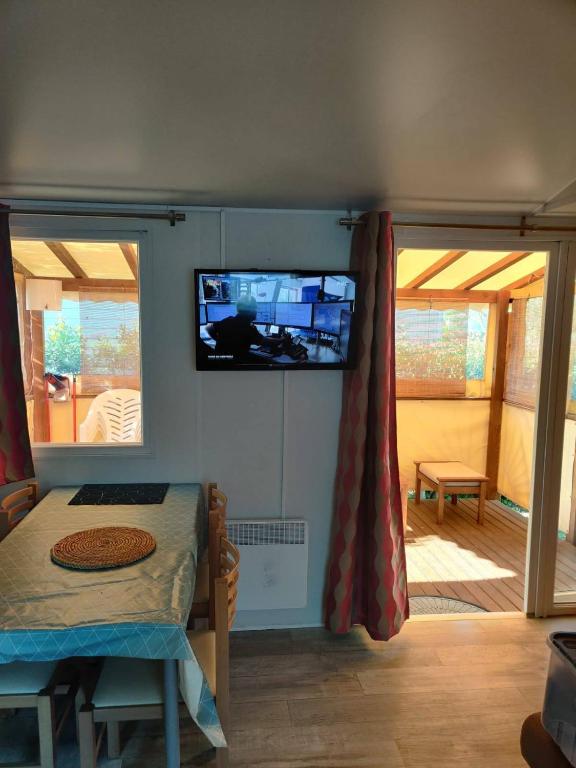a room with a tv on the wall and a table at MOBIL HOME CLIMATISE 2 CHAMBRES CLIMATISE CAMPING 4 ETOILES LE LAC DES REVES in Lattes