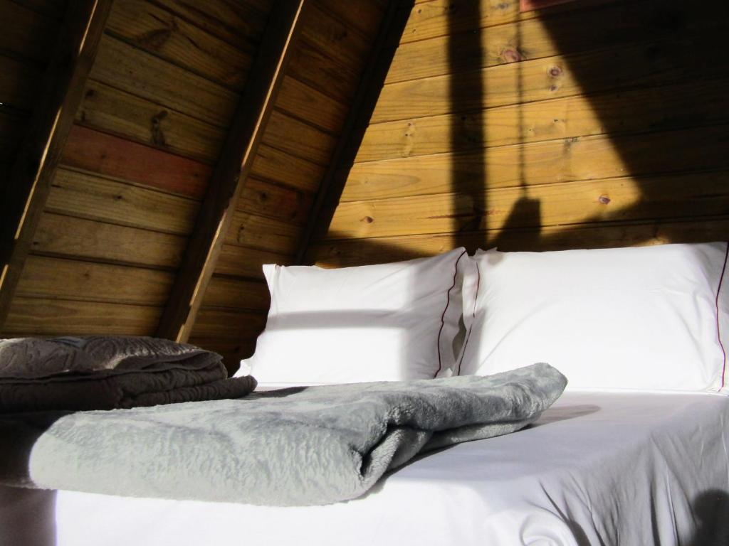 Bett mit weißer Bettwäsche und Kissen in einem Holzzimmer in der Unterkunft Chalé Cachoeira do Túnel- Linda vista da Serra da Mantiqueira in Delfim Moreira