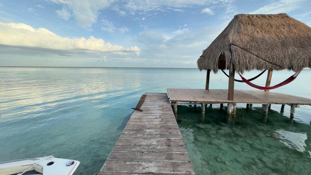 a pier with a straw umbrella and the water at Luigi's Glamping in Bacalar