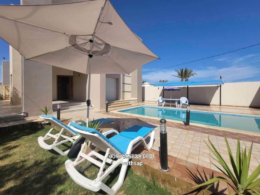 a pair of chairs and an umbrella next to a swimming pool at VILLA AZDEN in Al Maqārisah