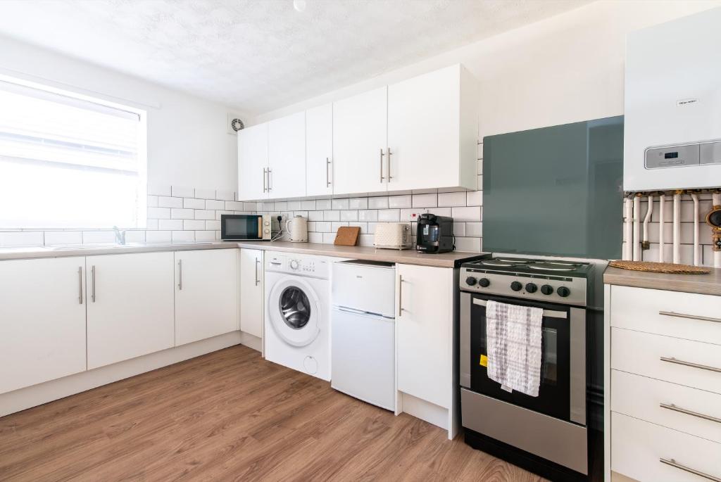 cocina con armarios blancos, lavadora y secadora en South Street Apartments, en Derby