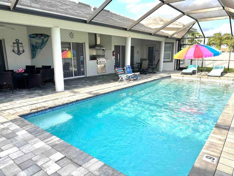 a swimming pool with two chairs and an umbrella at Tranquil & Inviting! 4BR, 2.5BA heated pool home! in Cape Coral