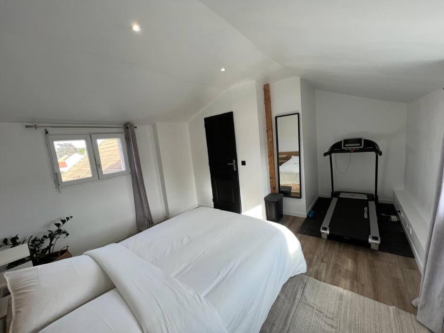 a bedroom with a white bed and a treadmill at Maison cocooning Porcheville 
