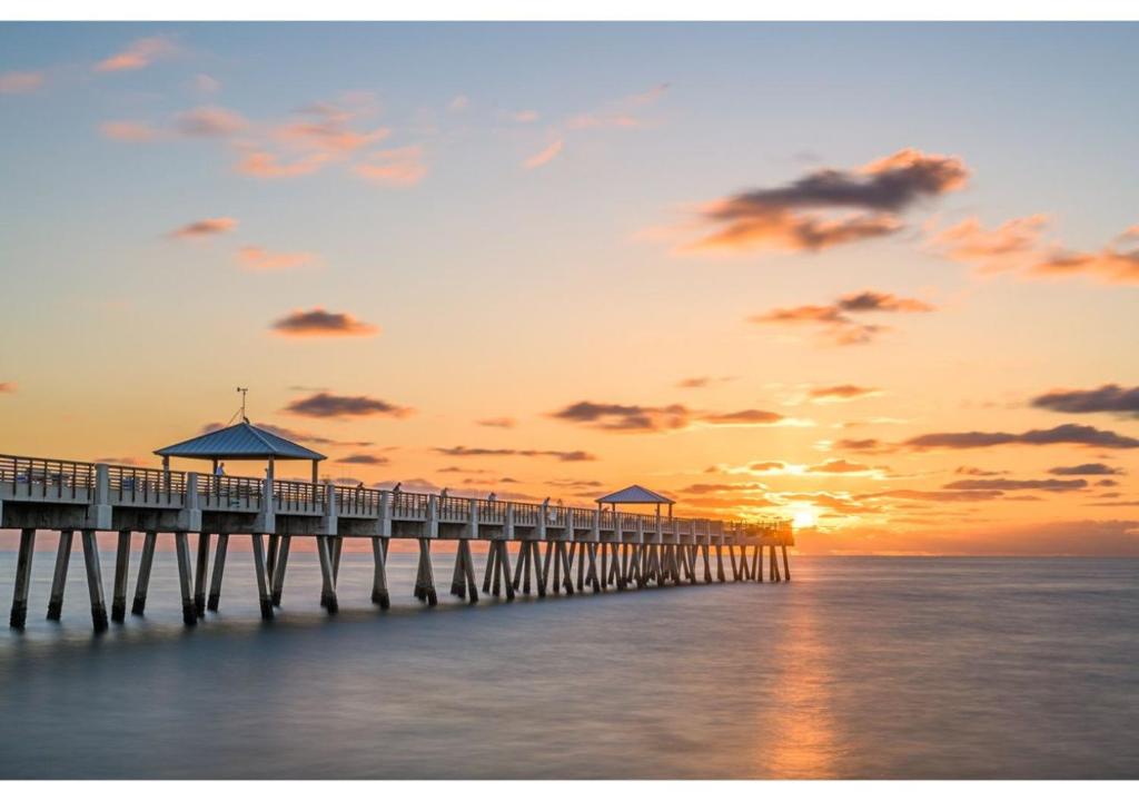 ein Pier, der sich bei Sonnenuntergang bis zum Meer erstreckt in der Unterkunft Discover the Charm and the Sea Gardens, an Exceptional Gold Coast Studio Condo Retreat - Special Offer Now! in Pompano Beach