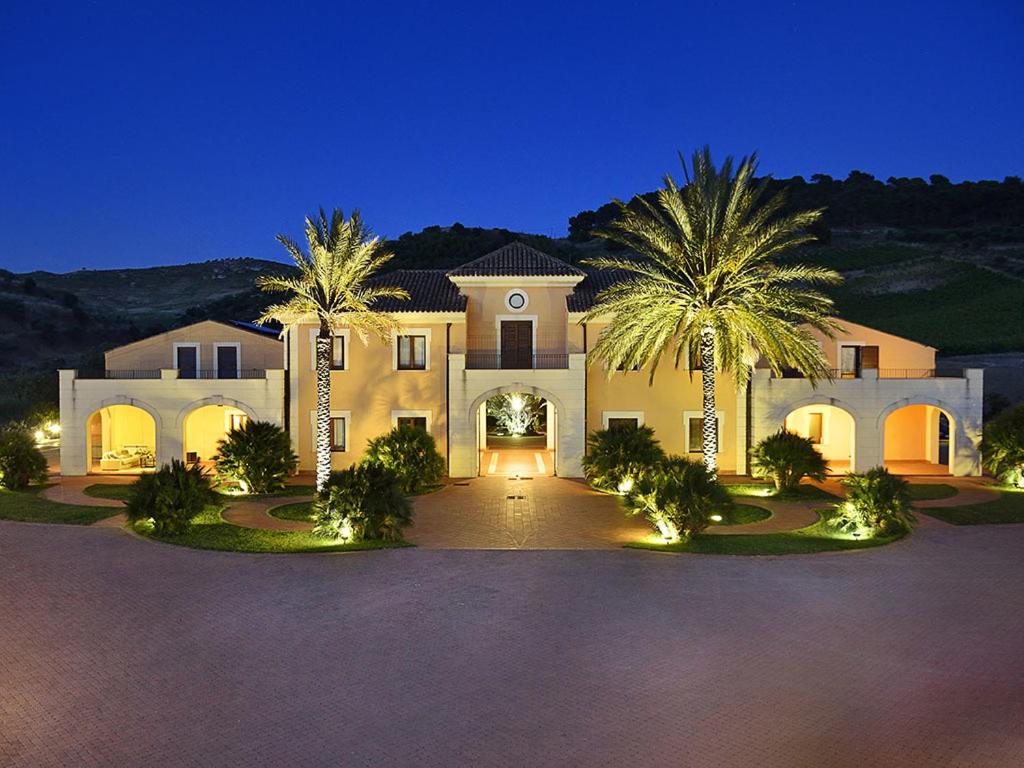 a large house with two palm trees in a driveway at Baglio Caruana Cantina & Relais in Montallegro