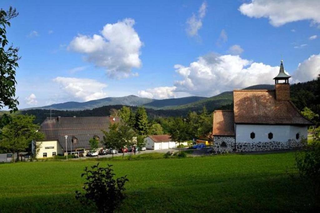 un grand champ verdoyant avec un bâtiment et une église dans l'établissement Berggasthof Lusen, à Neuschönau