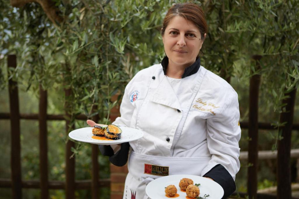 Uma mulher tem dois pratos de comida na mão. em Il Vecchio Frantoio em Stella Cilento