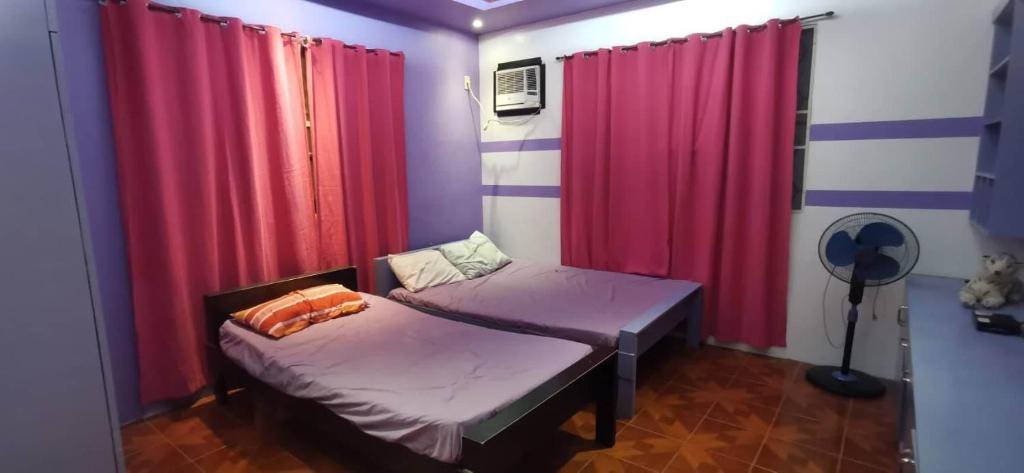 GG Resort في Dalumpinas Oeste: سريرين في غرفة مع ستائر حمراء وأرجوانية