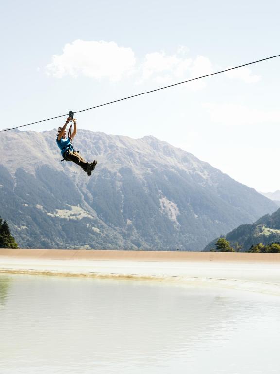 a man on a rope over a body of water at Falkensteiner Family Hotel Montafon - The Leading Hotels of the World in Schruns-Tschagguns