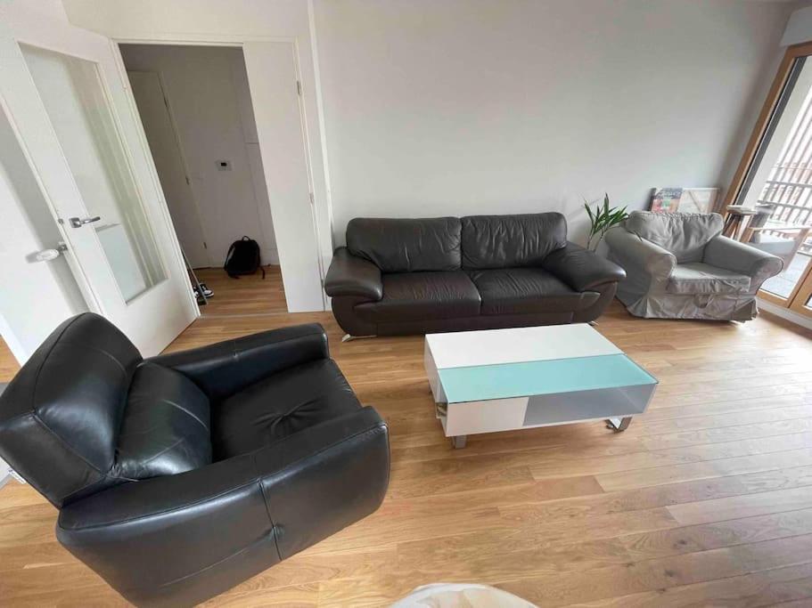 a living room with a black leather couch and a coffee table at Magnifique logement avec terrasse &amp; climatisation in Aubervilliers