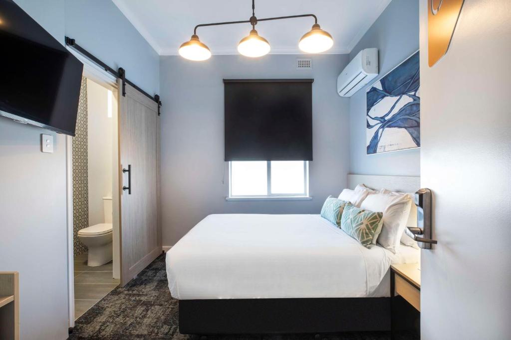 a small bedroom with a bed and a bathroom at Nightcap at Rex Hotel in Adelaide