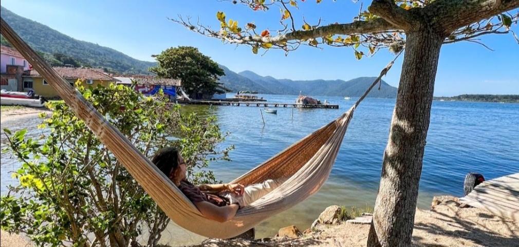 Ein Mann, der in einer Hängematte neben einem See liegt. in der Unterkunft Refugio Bela Ilha via Barco in Florianópolis