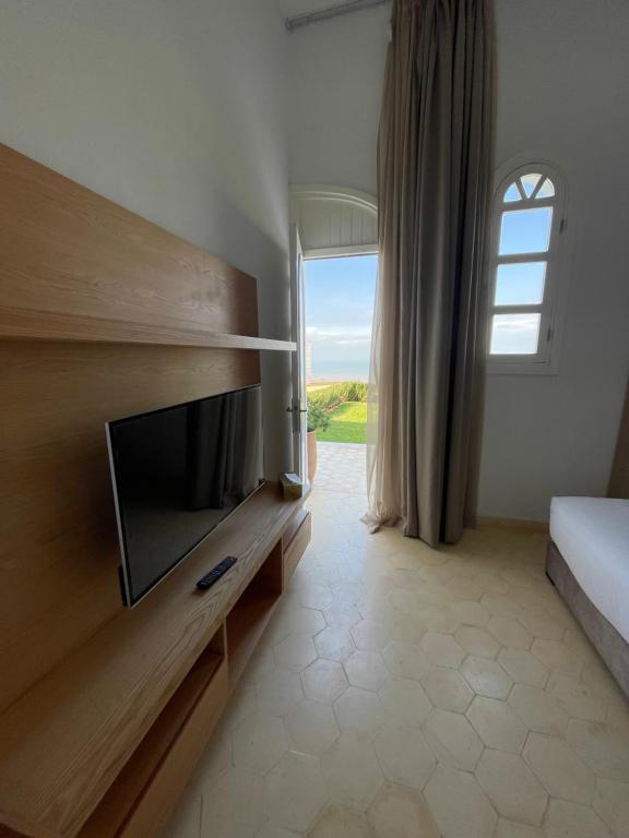a bedroom with a tv and a bed and a window at Villa La Falaise in Oualidia