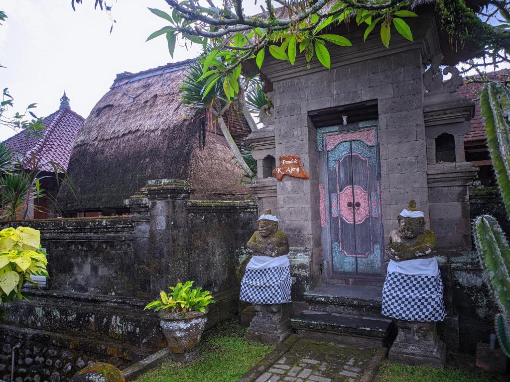 zwei Statuen vor einem Haus mit einer Tür in der Unterkunft K'Ajeng Cottage in Penebel