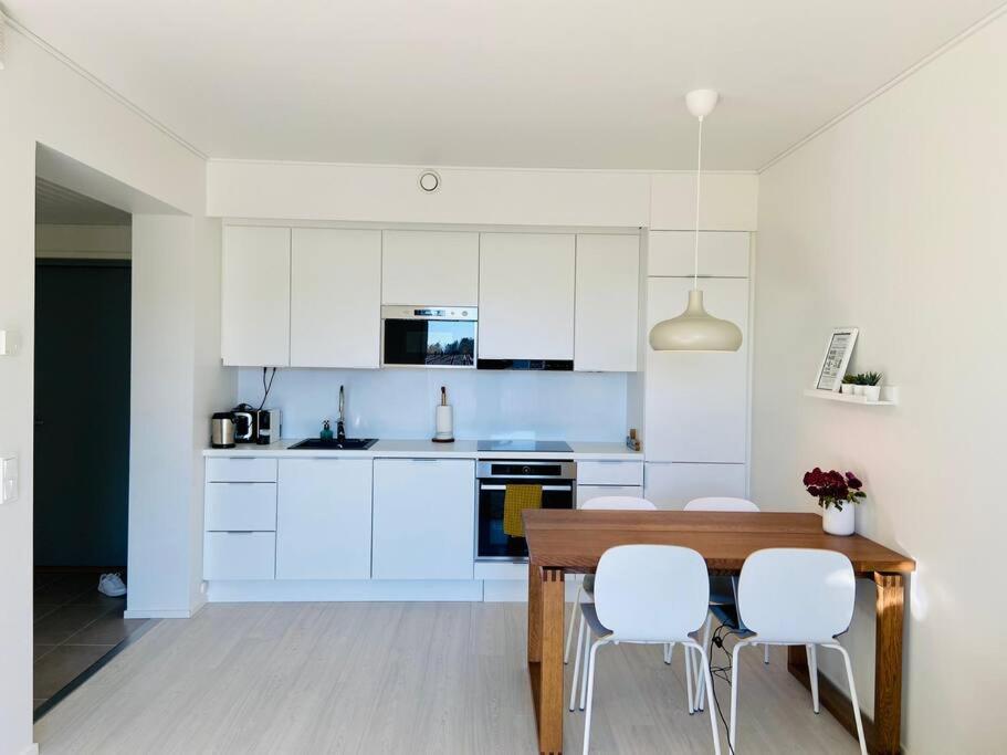 a kitchen with white cabinets and a wooden table and chairs at Lakeside Modern Minimalist Apartment FreeParking in Järvenpää