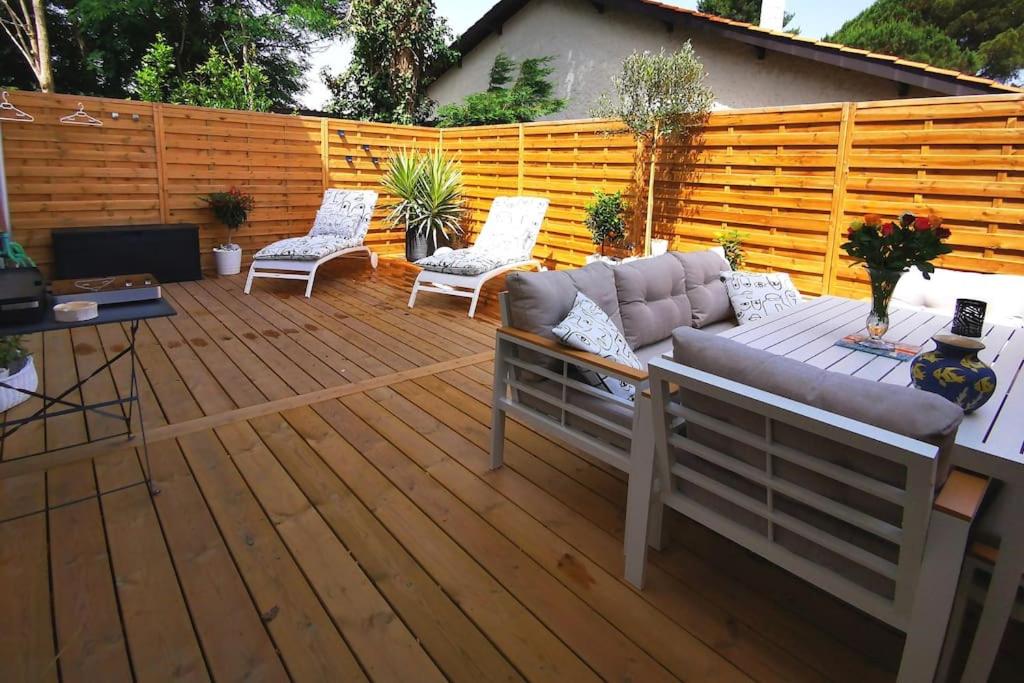 eine Terrasse mit einem Sofa und Stühlen auf einer Holzterrasse in der Unterkunft Maison de vacances chaleureuse à 600mdu Bassin in Andernos-les-Bains