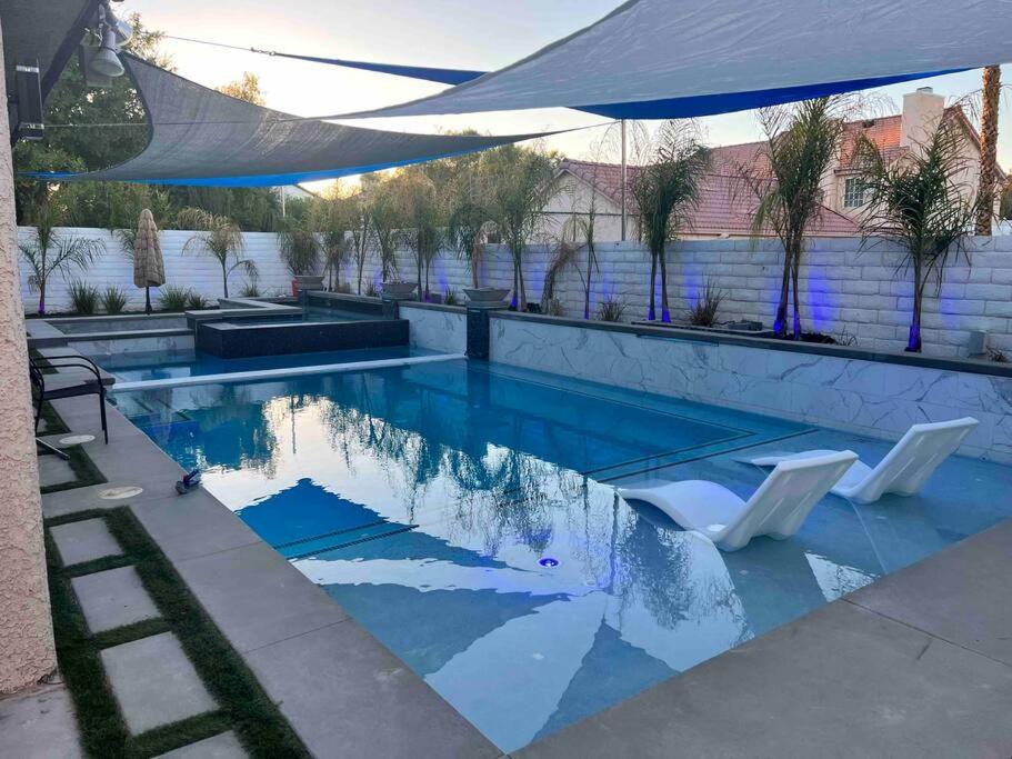 a swimming pool with two white chairs and an umbrella at Plush Las Vegas Retreat 5 min from Strip in Las Vegas