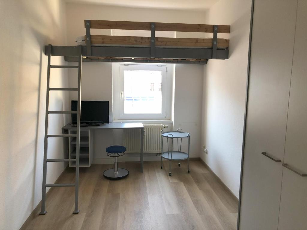 a loft bed with a desk and two stools in a room at Ferienwohnung am Marienplatz in Görlitz