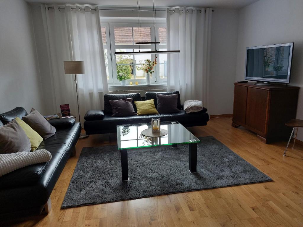 ein Wohnzimmer mit einem schwarzen Sofa und einem Glastisch in der Unterkunft Ferienwohnung Schöpstalblick in Ebersbach