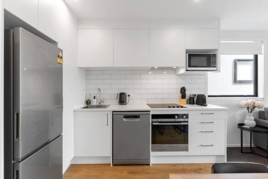 La cuisine est équipée de placards blancs et d'un réfrigérateur en acier inoxydable. dans l'établissement Contemporary Urban Retreat, à Auckland