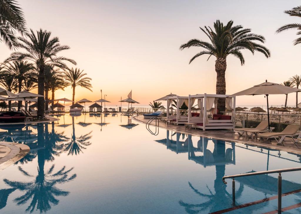 una piscina en un complejo con palmeras y sombrillas en TUI BLUE Scheherazade Adults Only en Sousse