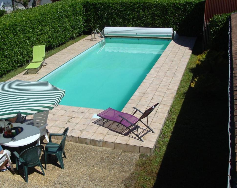 a swimming pool with chairs and a table and an umbrella at Les tilleuls in Soustons