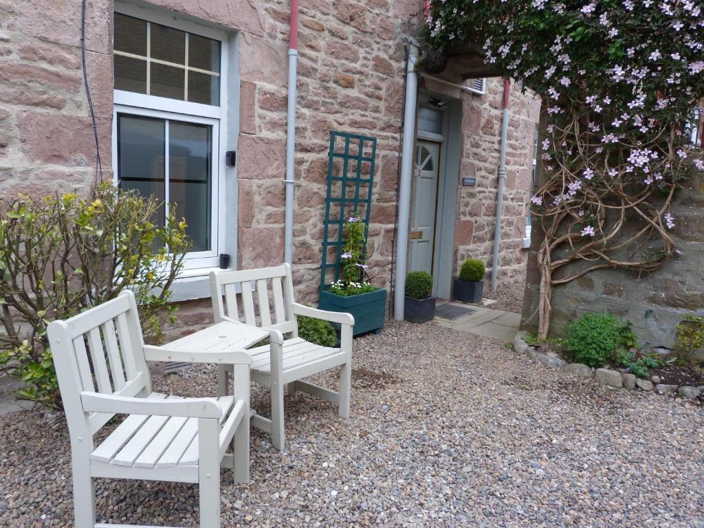 two white chairs and a table in front of a house at Wee Ness Cottage in Inverness