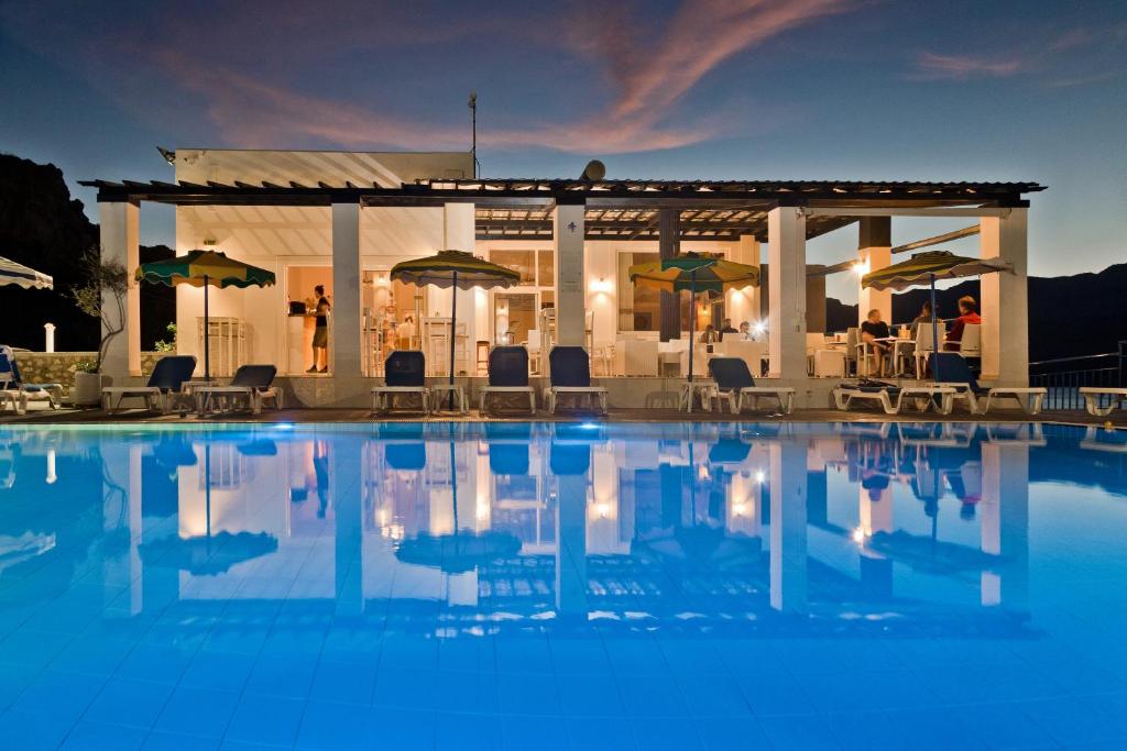 una piscina con sillas y sombrillas frente a un edificio en CHC Sound of the Sea, en Karpathos