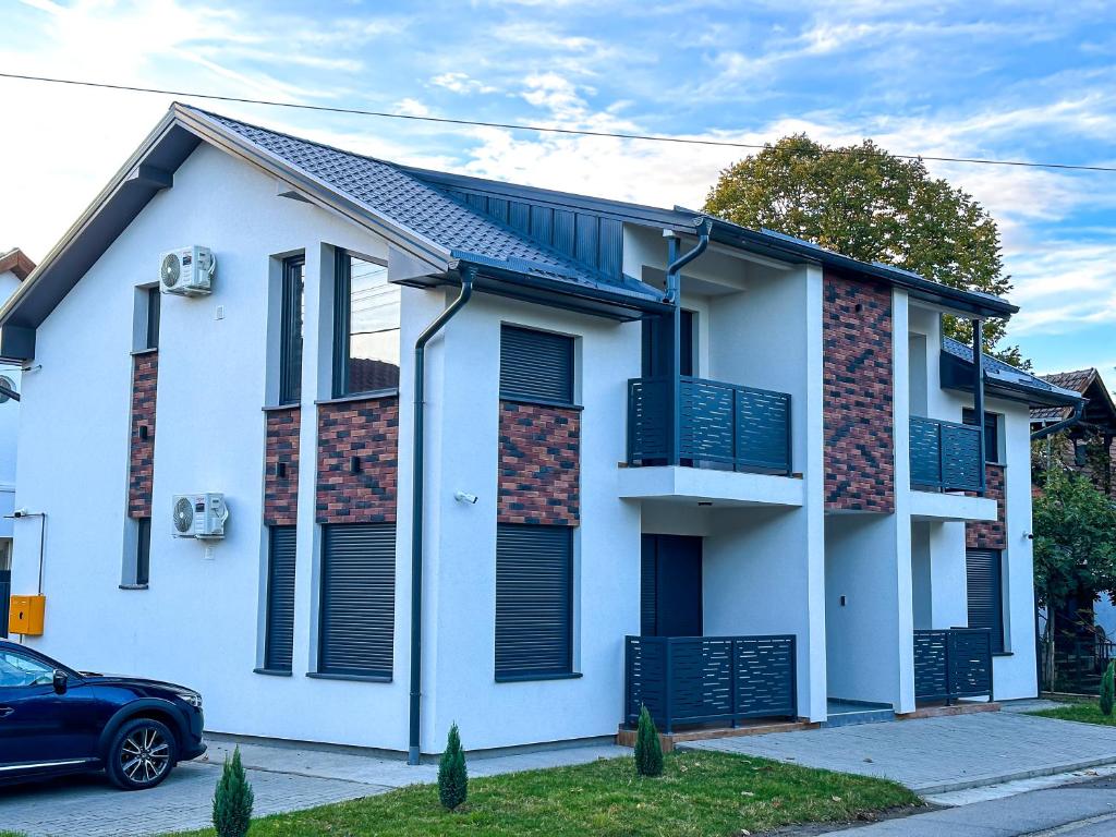 a white house with black shutters and a blue car at Kiko apartmani LUX in Zrenjanin