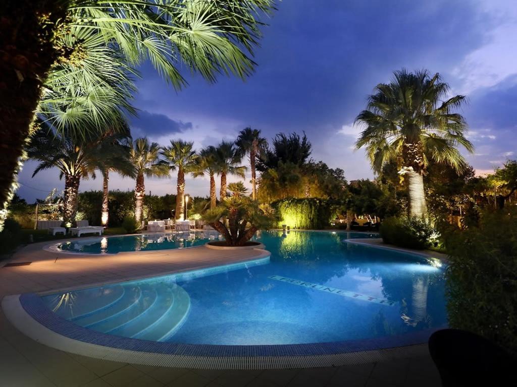una piscina por la noche con palmeras y luces en Masseria La Brunetta, en Massafra