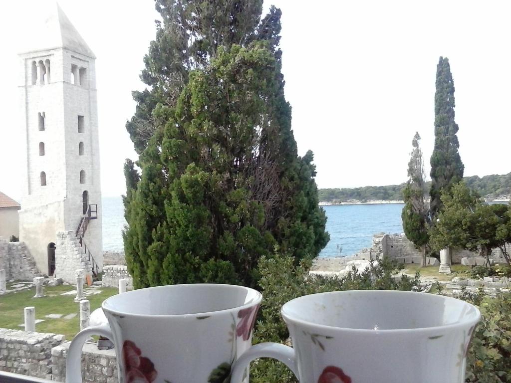 two cups on a window sill with a view of the water at Apartments Zlata In the Heart of the Old Town, Close to the Beach in Rab