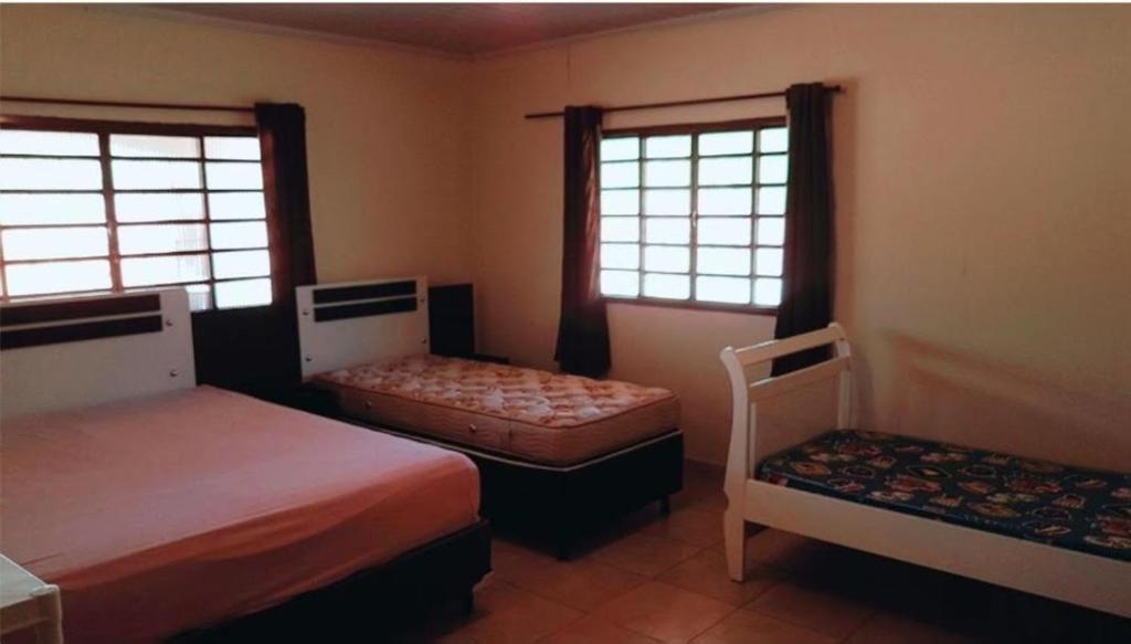 a bedroom with two beds and a chair and two windows at Fazenda Araras Pirenópolis in Pirenópolis