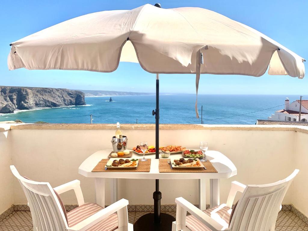 a table with a plate of food and an umbrella at Apartment Praia Arrifana with BALCONY and SEA VIEW in Aljezur