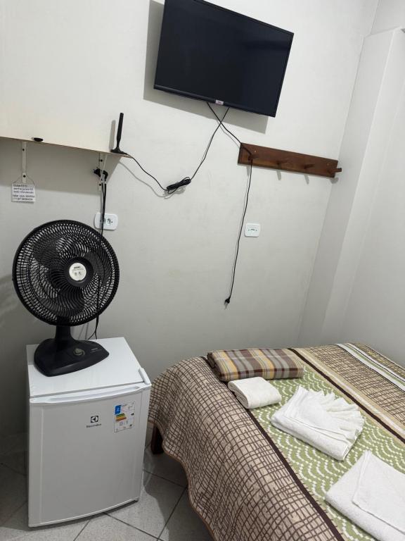 a room with a bed with a fan and a tv at Quarto Laurinda 3 in Guararema
