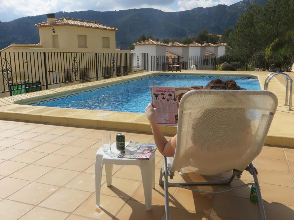 a person sitting in a chair reading a book by a pool at *Casa Anna L'Atzubia in Adsubia