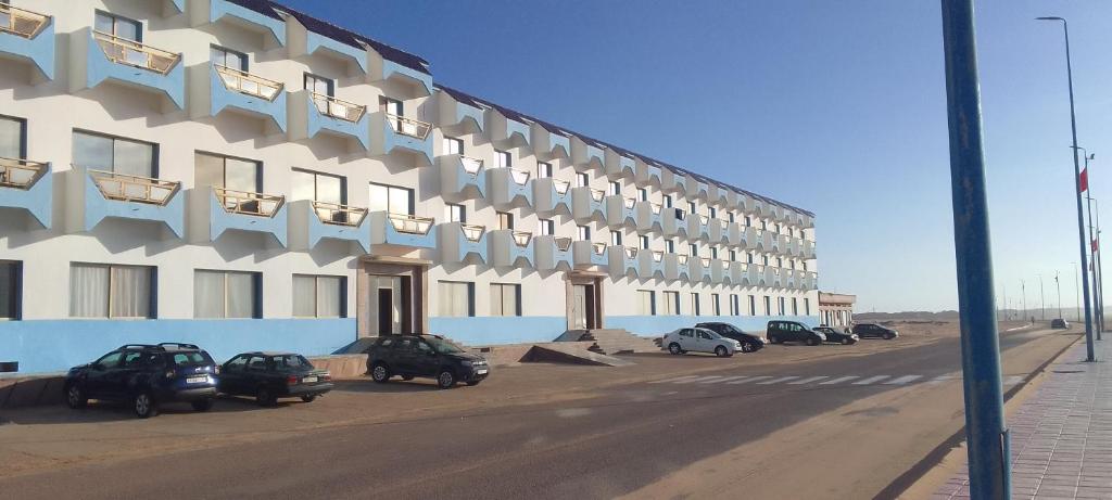 um grande edifício com carros estacionados em frente em HOTEL NAGJIR PLAGE em Laayoune