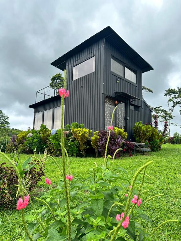 a black tiny house in a field with pink flowers at Alto Luciérnaga 