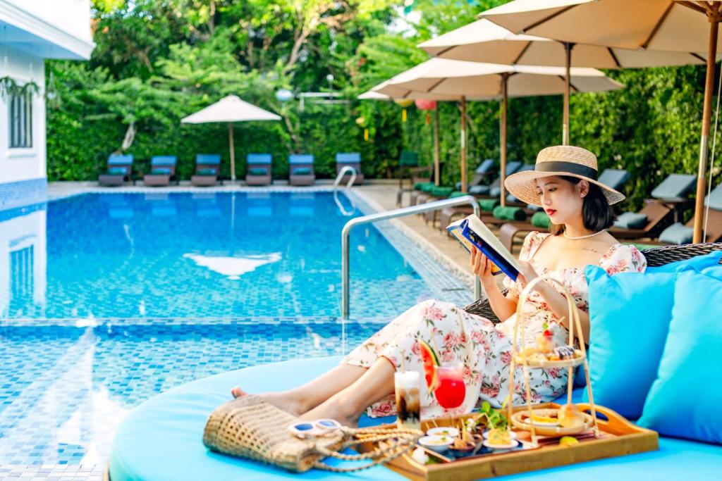 a woman sitting in a chair reading a book by a pool at Wyndham Garden Hoi An Cua Dai Beach in Hoi An