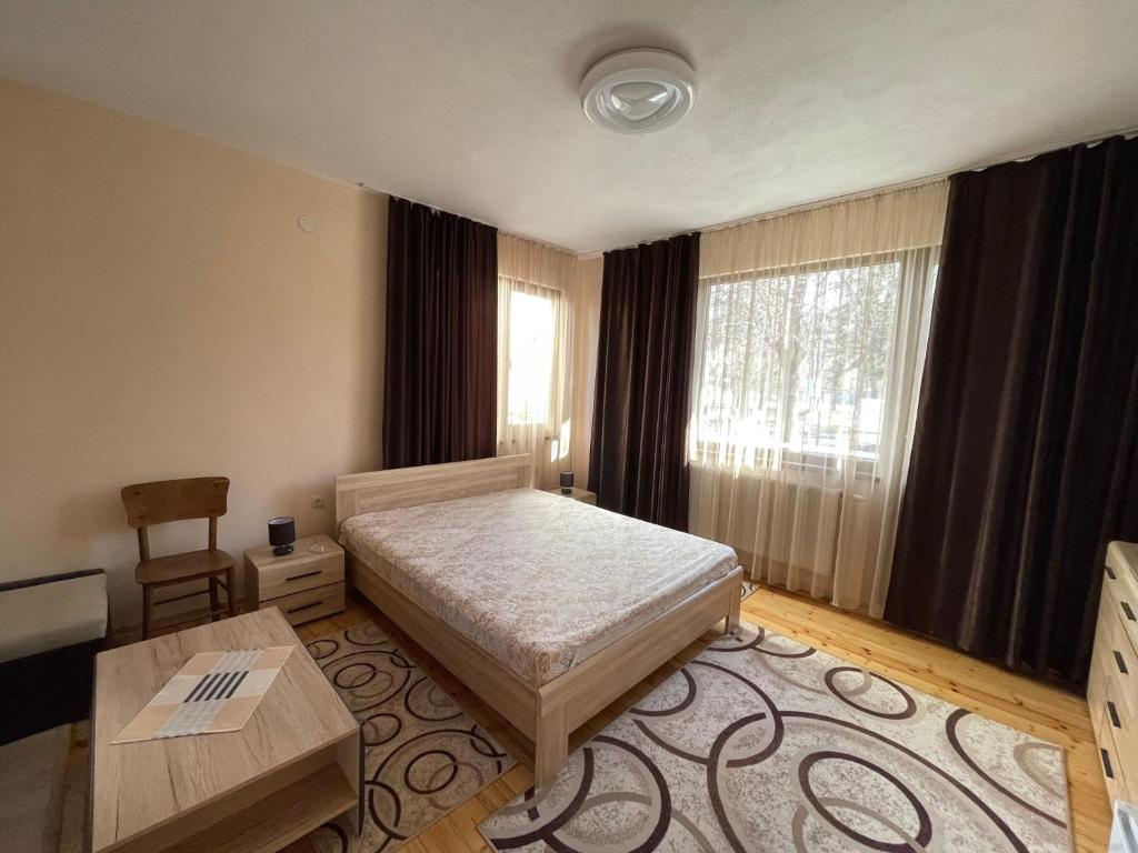 Un dormitorio con una cama y una mesa y ventanas. en The Chestnut Apartments - Апартаменти Кестените, en Velingrad