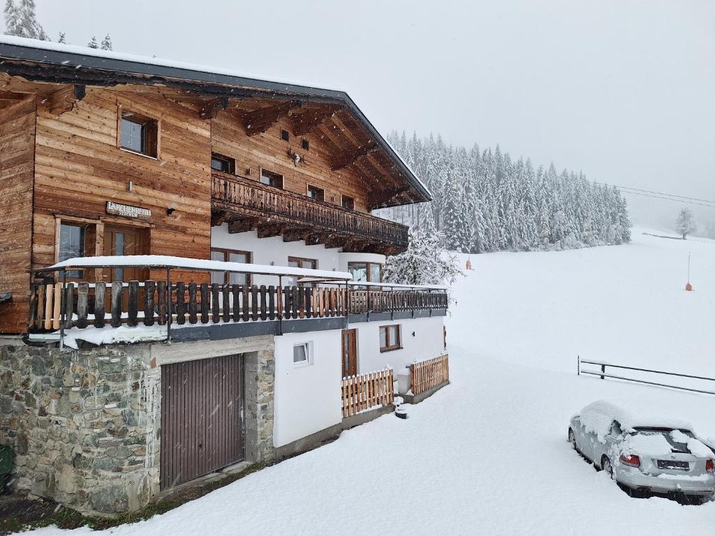 a log cabin with a car parked in the snow at Lärchenreith Appartement in Schladming