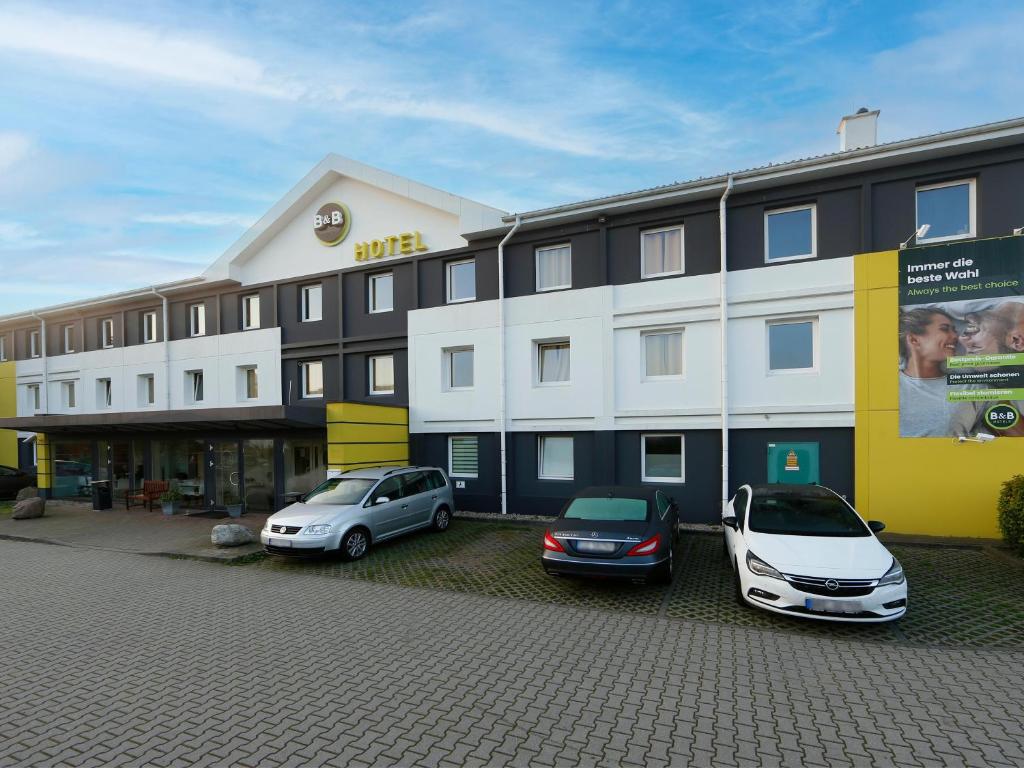 dos coches estacionados frente a un gran edificio en B&B Hotel Berlin-Süd Genshagen, en Ludwigsfelde