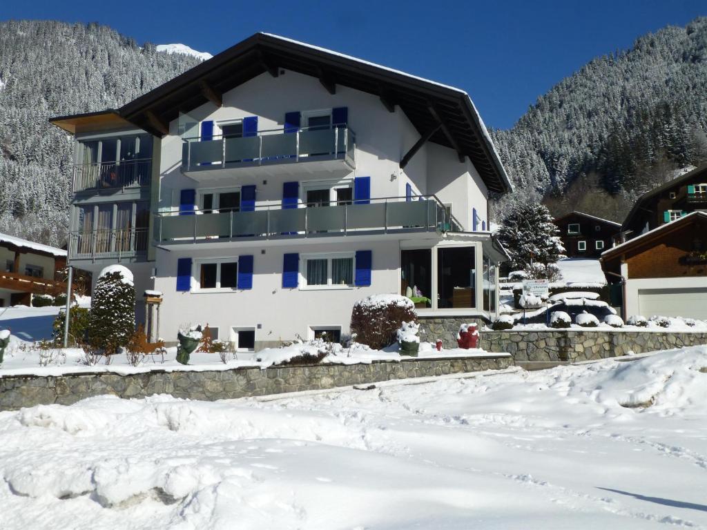 a white house with blue windows in the snow at Appartement Zint in Sankt Gallenkirch