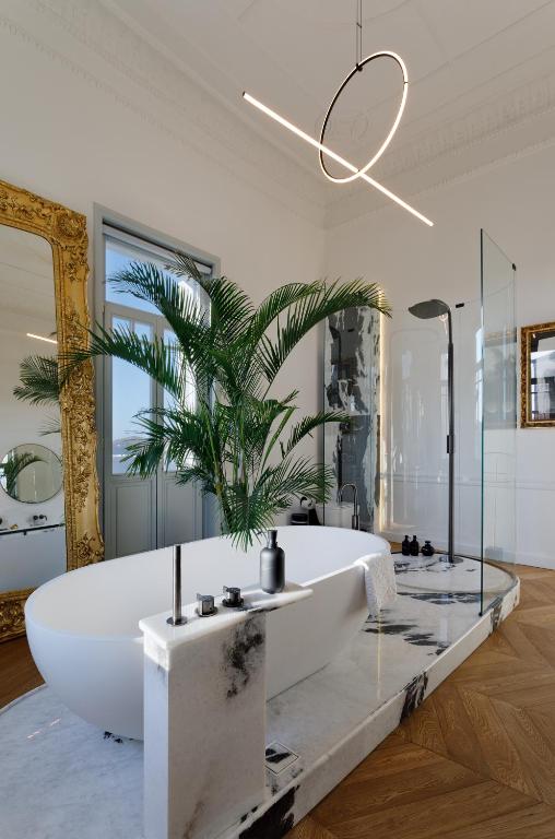 a bathroom with a large white tub and a palm tree at Aristide Hotel - Small Luxury Hotels of the World in Ermoupoli