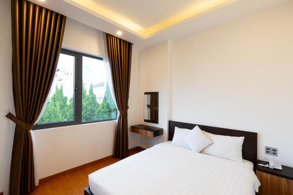 a bedroom with a white bed and a large window at TTR Midtown View Hotel in Da Lat