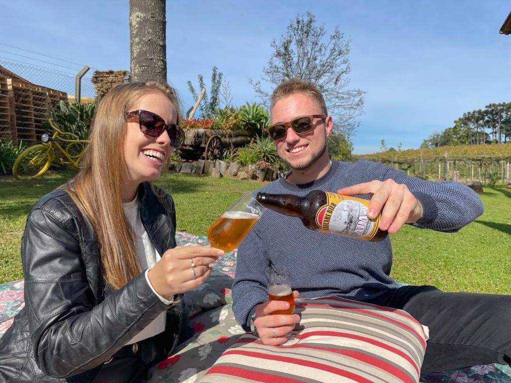 Un uomo e una donna seduti su una coperta che bevono birra di Cabana Aconchego do Recanto a São Valentim do Sul