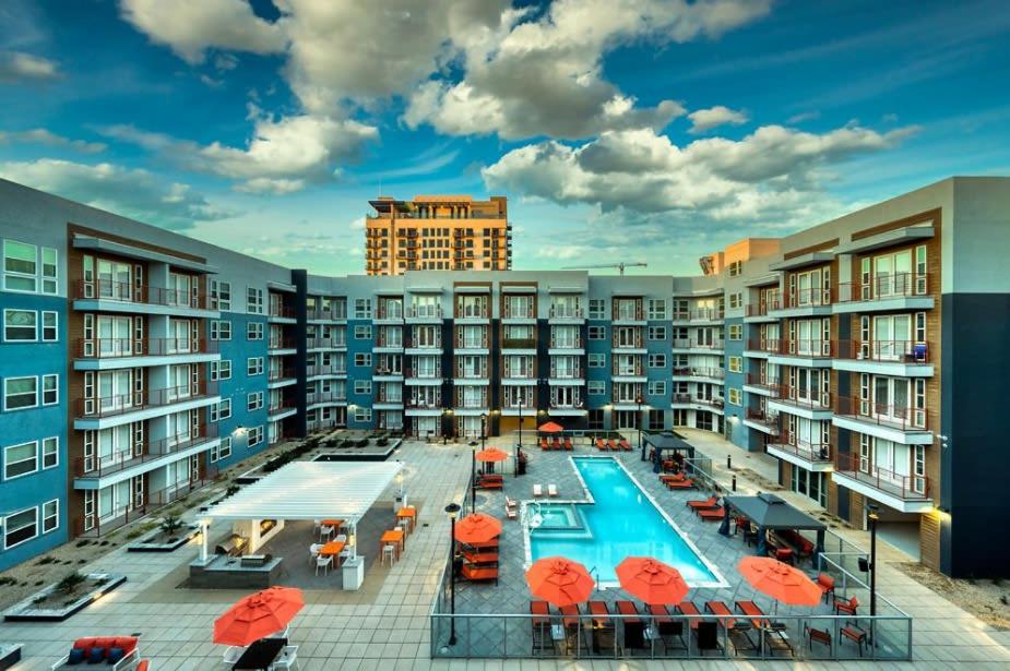 an apartment complex with a swimming pool and orange umbrellas at Cozysuites PHX RORO Gym, Pool, Pets, Parking! #9 in Phoenix